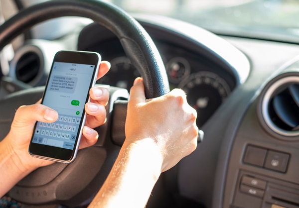 A driver types a text message on a smartphone while holding the steering wheel, a dangerous behavior that often leads to fatal distracted driving accidents in Houston.